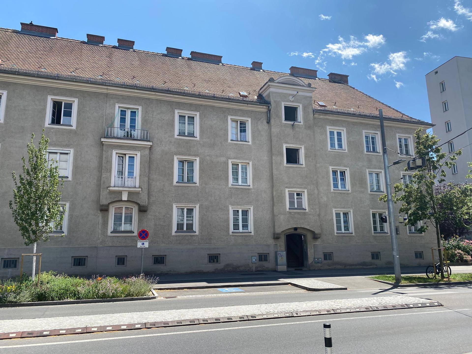 Klassische Wohnhausfassade mit vielen Fenstern, einem kleinen Balkon und Satteldach an einer Straße.