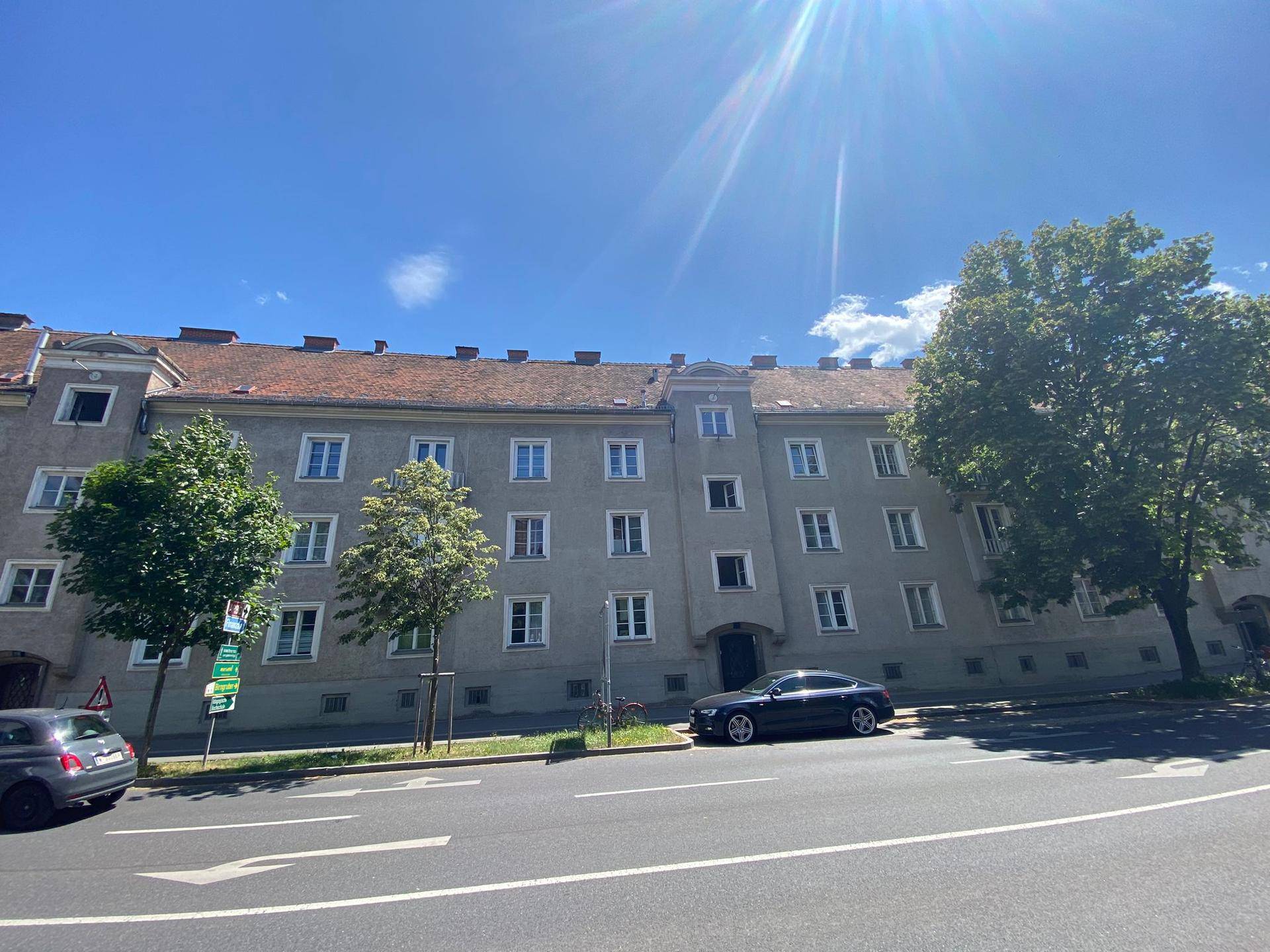 Mehrstöckiges Wohngebäude mit klassischer Fassade, vielen Fenstern und Satteldach an einer sonnigen Straße.