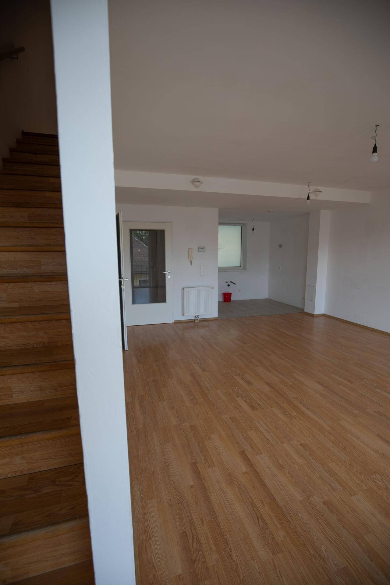 Geräumiger Wohnbereich mit Holzboden und einer Holztreppe, die in eine obere Etage führt.