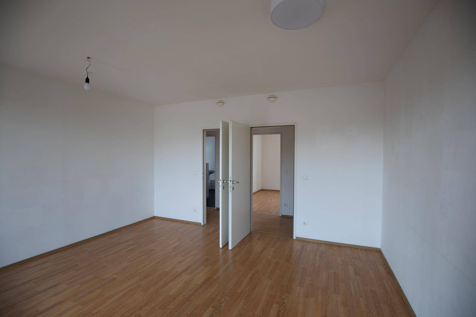 Helles, leeres Zimmer mit Holzboden und Doppeltüren, das vielseitig genutzt werden kann.