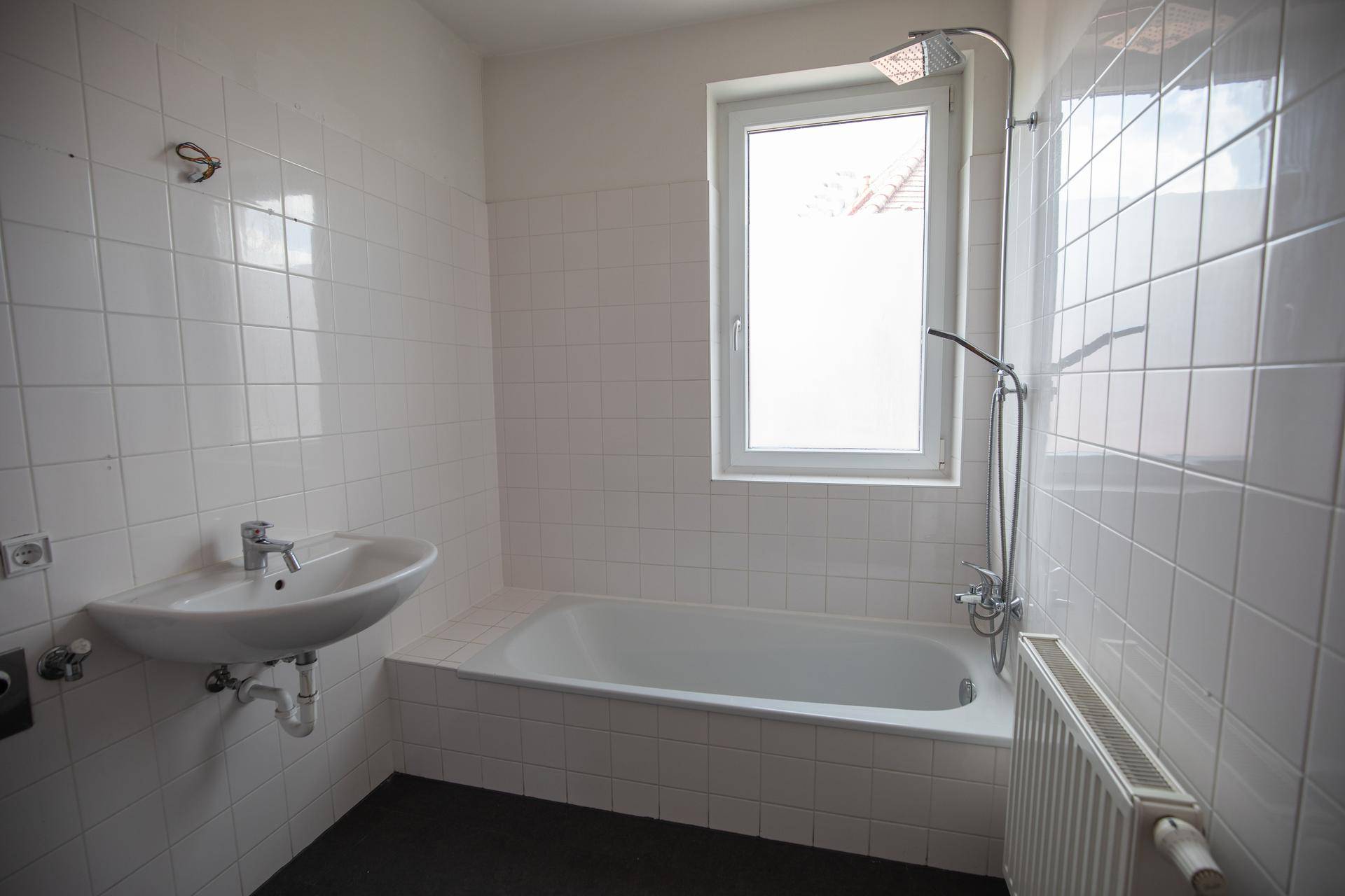 Badezimmer mit Badewanne, Duschfunktion, Waschbecken und weißen Wandfliesen.