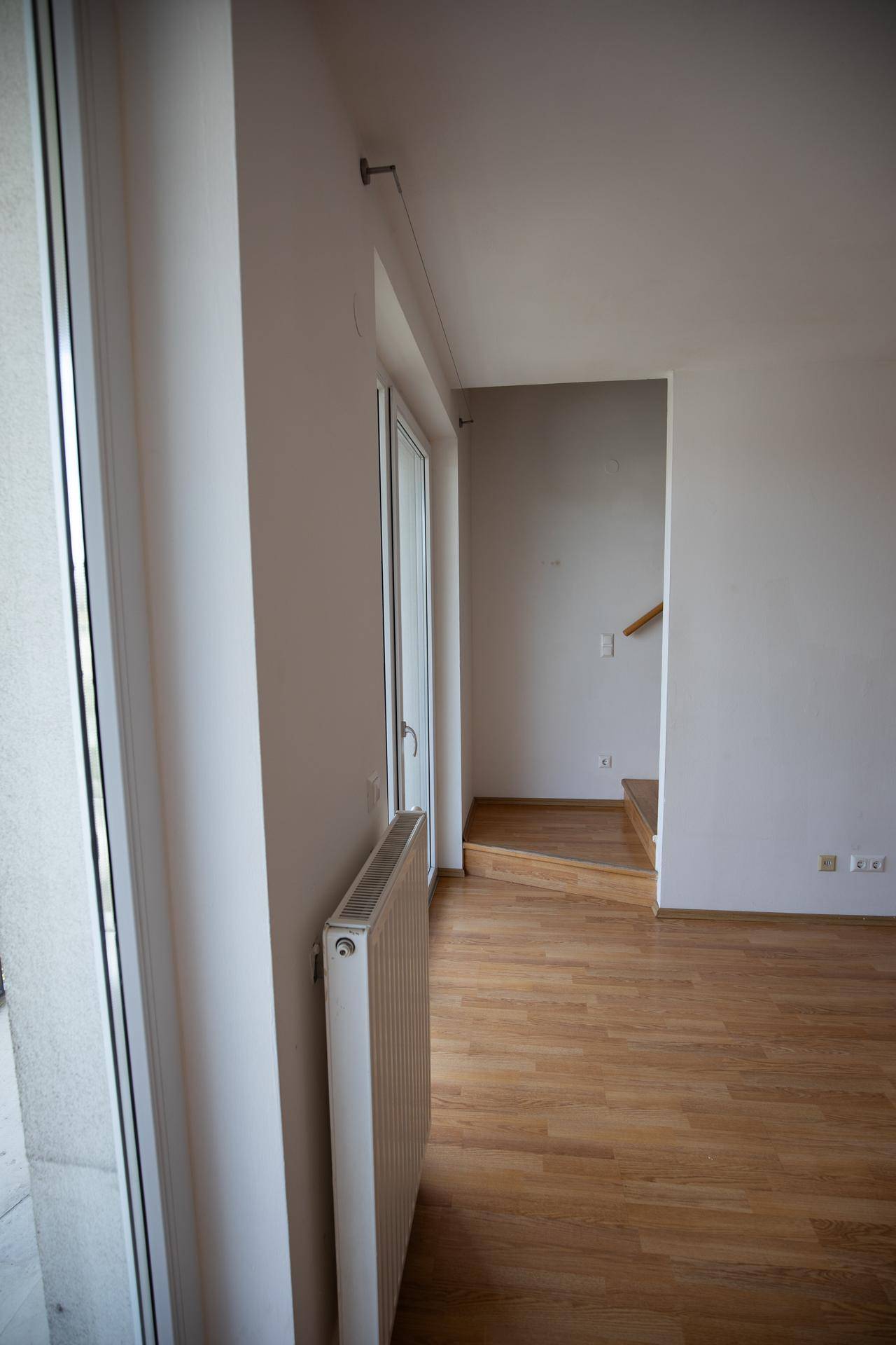 Heller Wohnbereich mit Holzboden, Zugang zum Balkon und einer Treppe.