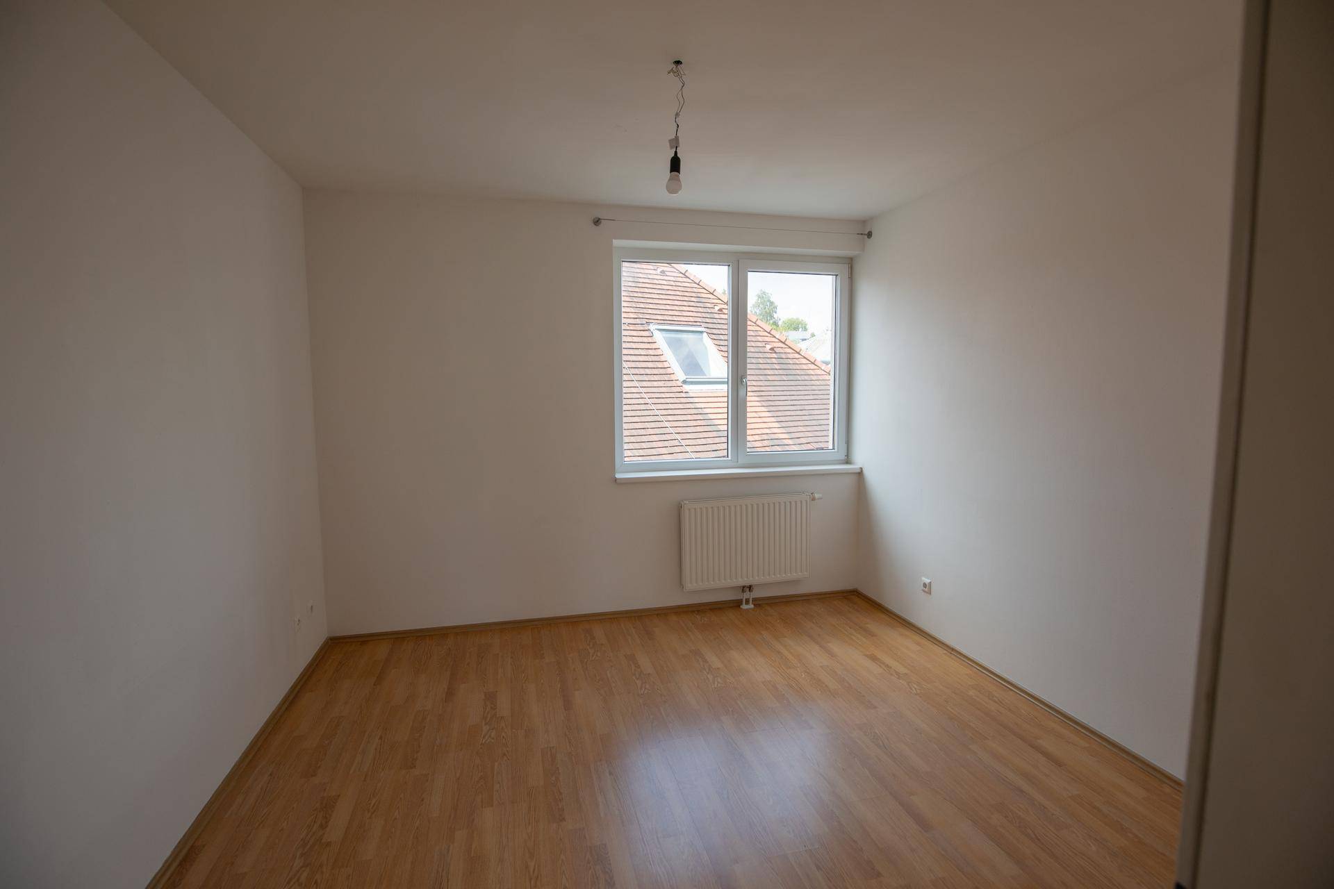 Leeres Schlafzimmer mit Holzboden und einem Fenster, das viel Tageslicht hereinlässt.