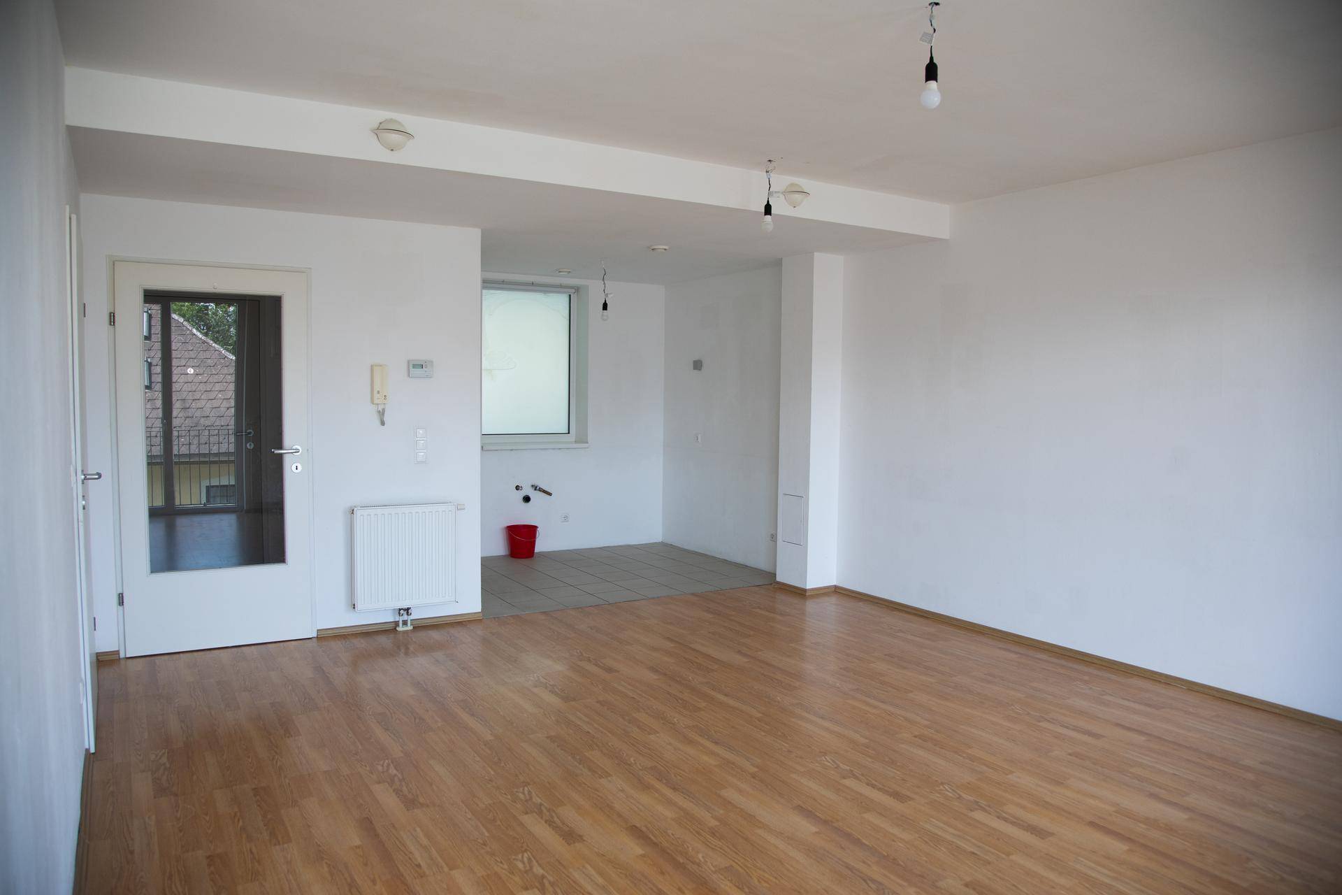 Geräumiger offener Wohnbereich mit Holzboden und einem gefliesten Bereich, ideal für eine Küche.