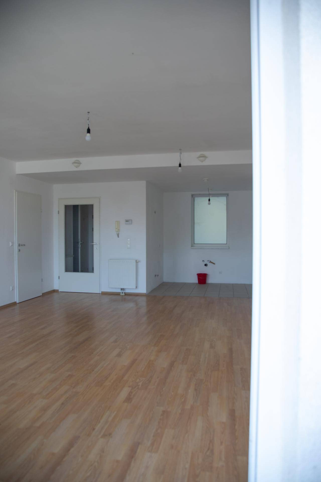 Großer, heller Wohnbereich mit Holzboden und einem gefliesten Bereich, ideal für eine offene Küche.