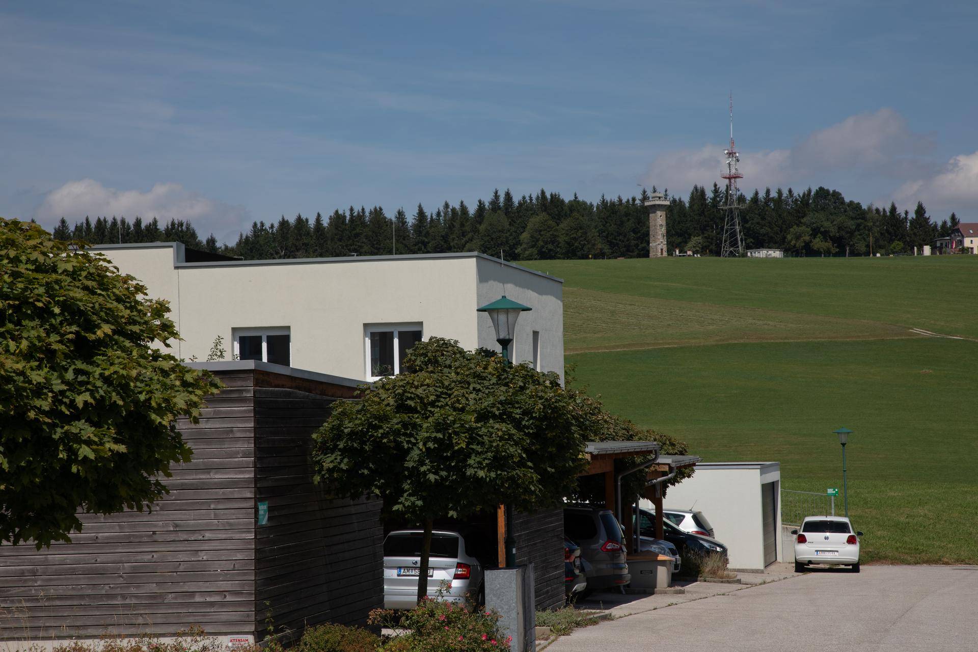 Moderne Gebäude mit Parkplätzen und einem weiten Blick auf grüne Hügel und einen Sendeturm.