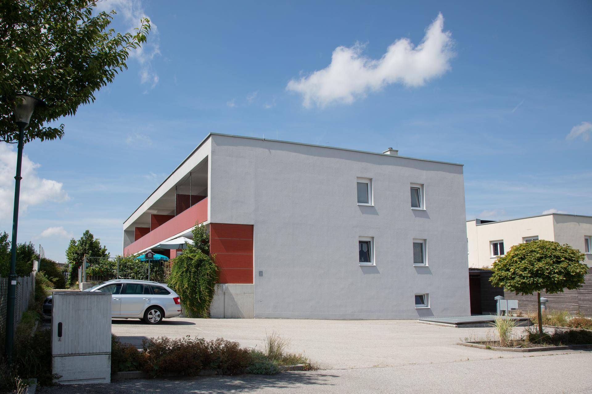 Modernes Wohngebäude mit weißer Fassade, roten Akzenten und Parkplätzen im Freien.