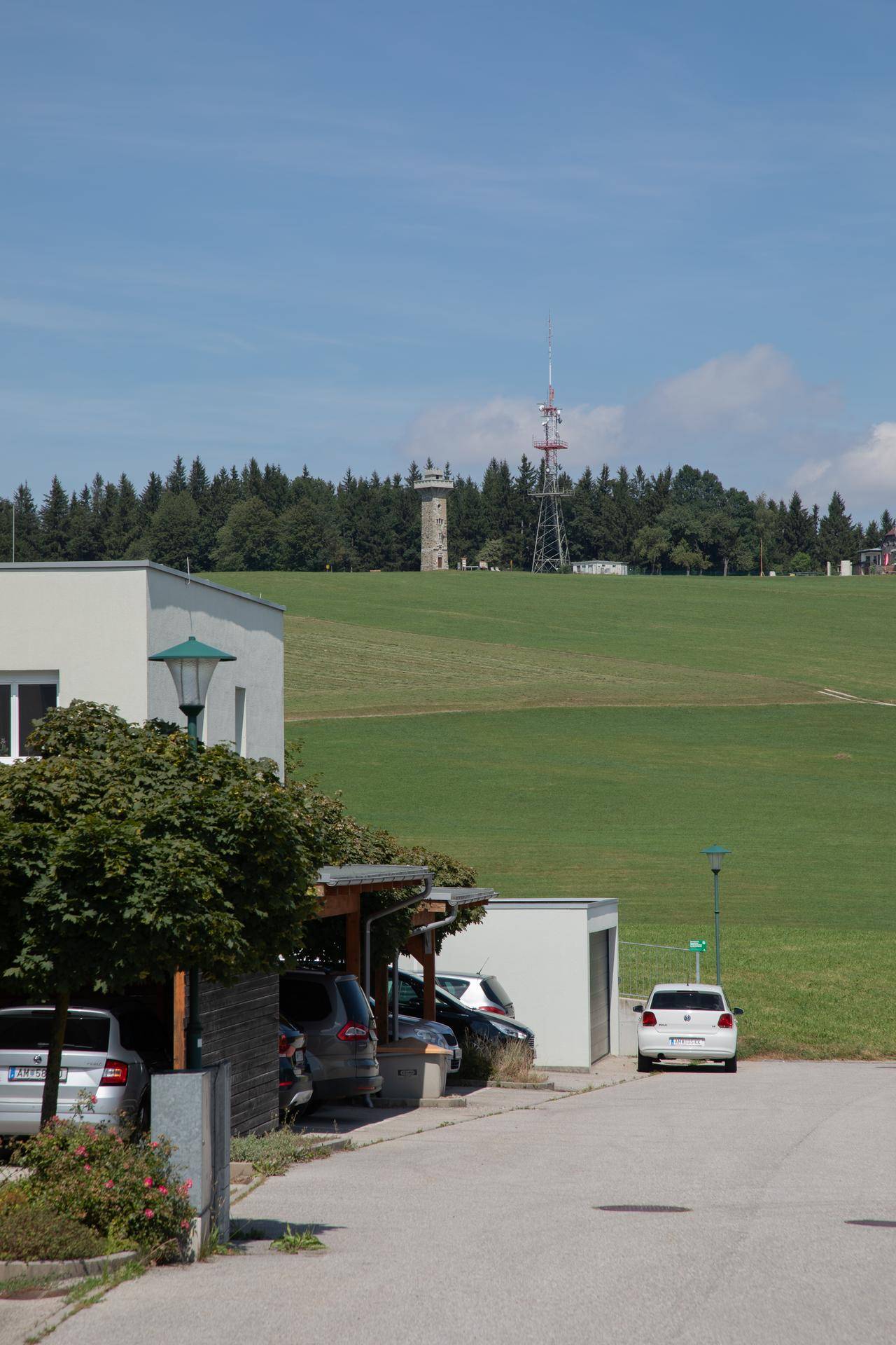 Moderne Gebäude mit Parkplätzen und einem weiten Blick auf grüne Hügel und einen Sendeturm.