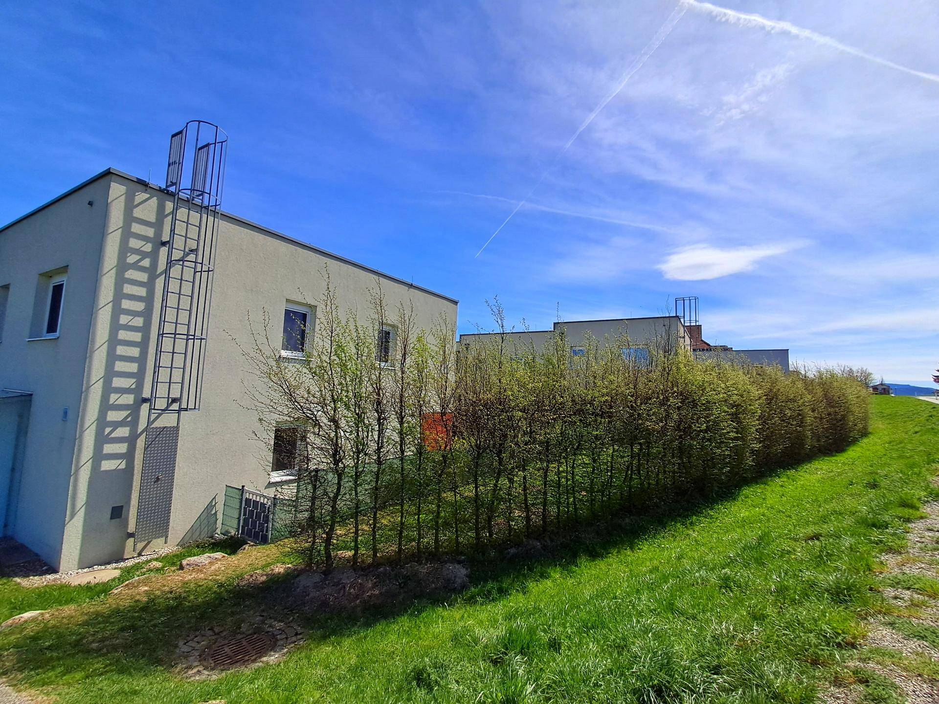 Moderne Wohngebäude mit heller Fassade und einer außenliegenden Leiter vor einem grünen Hang.