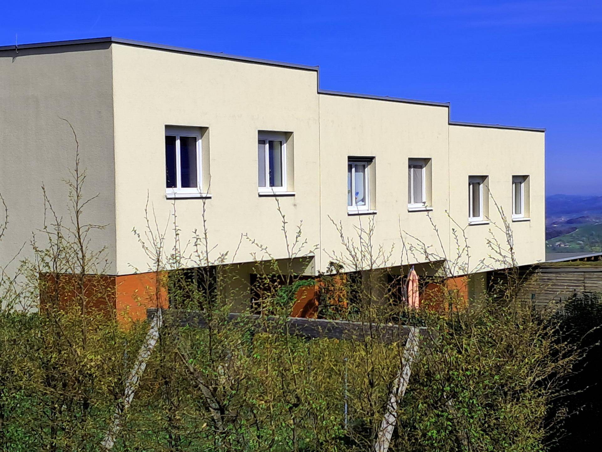 Reihenhäuser mit heller Fassade und roten Akzenten, umgeben von grüner Vegetation unter blauem Himmel.