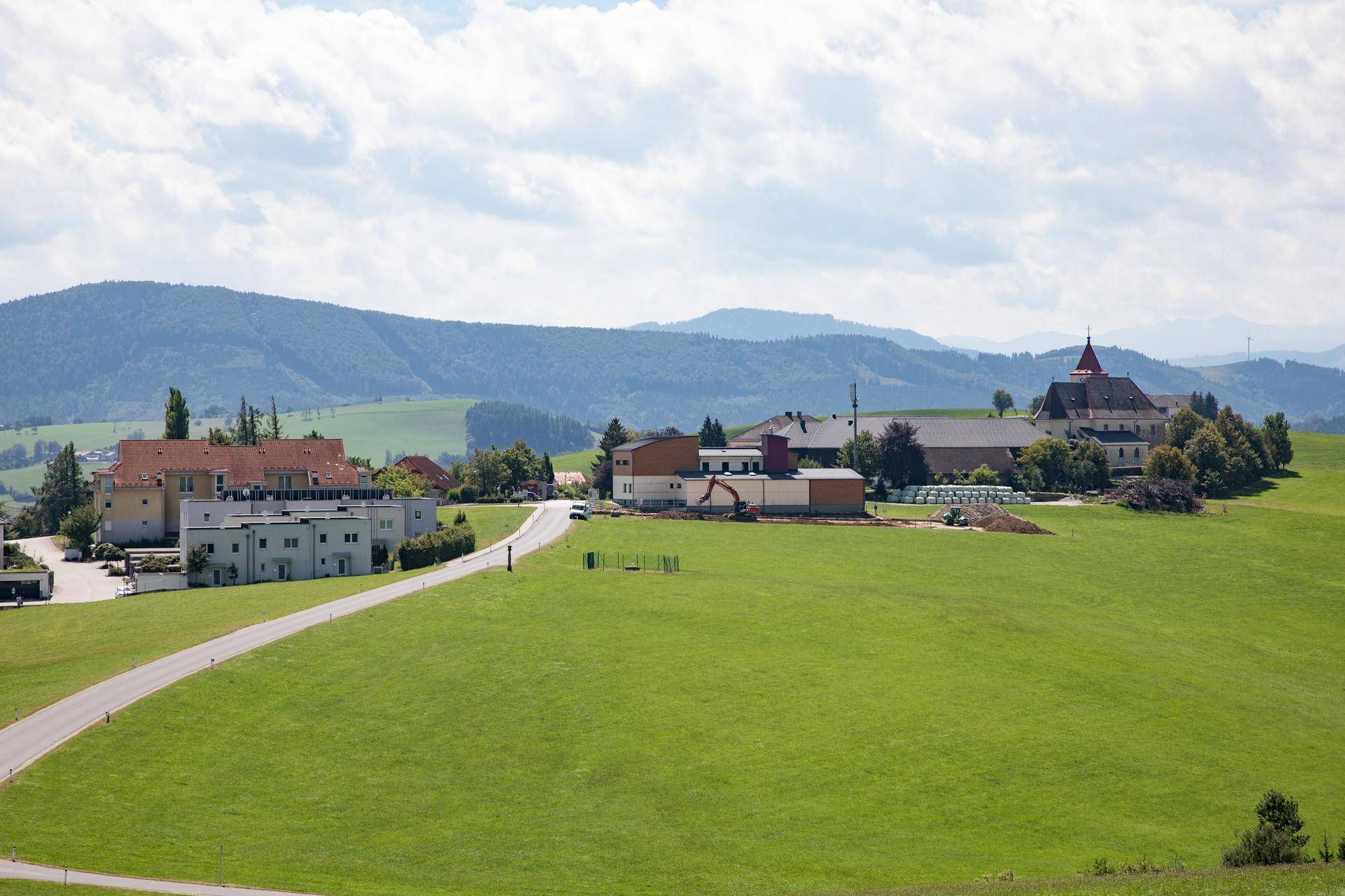 Weitläufige grüne Hügellandschaft mit einem Dorf und einer Kirche in der Ferne unter blauem Himmel.
