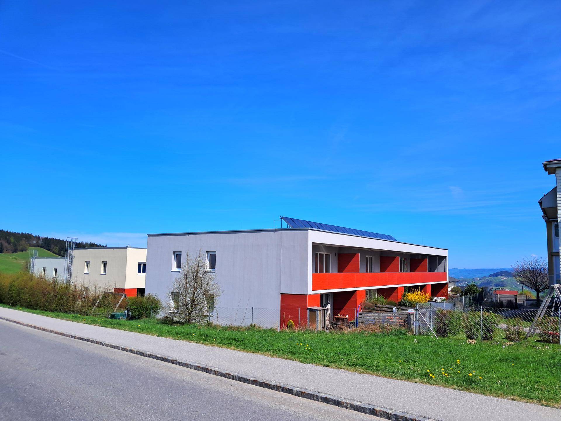 Modernes Wohngebäude mit roter Fassade und Photovoltaikanlage auf dem Flachdach.