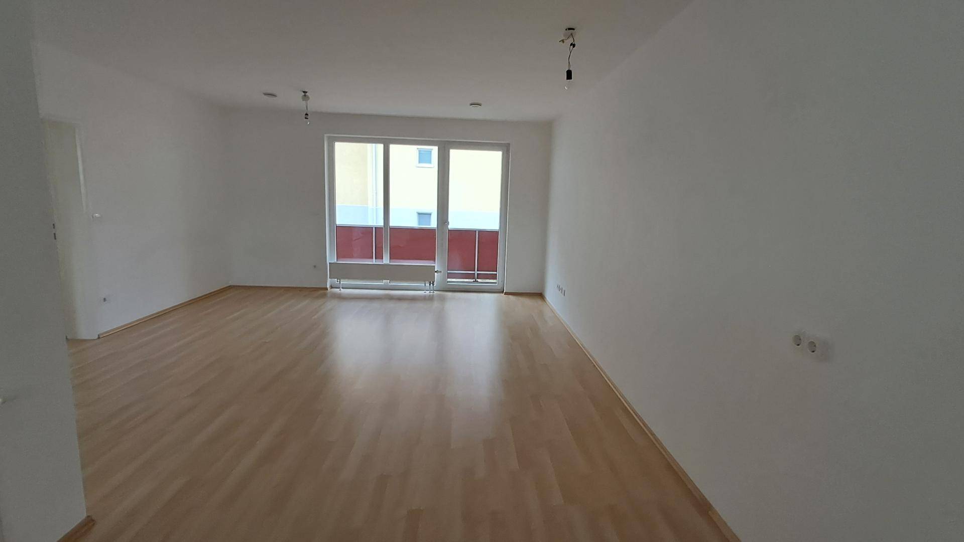 Geräumiger, heller Wohnbereich mit Laminatboden und großem Fenster mit Balkonzugang.