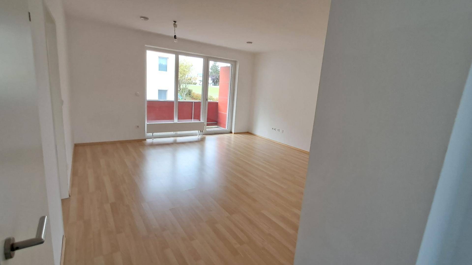 Heller Wohnbereich mit Laminatboden und großem Fenster, das viel Tageslicht hereinlässt.