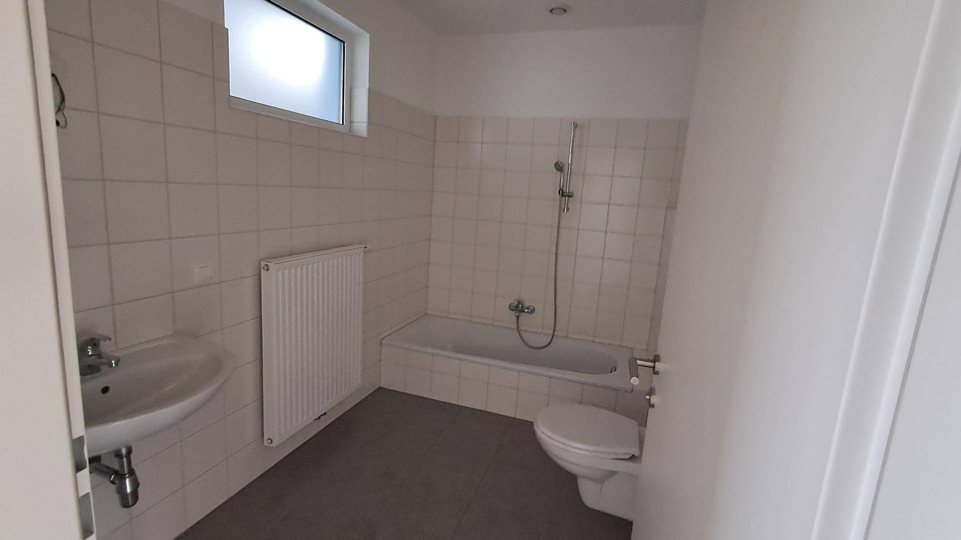 Helles Badezimmer mit Badewanne, Waschbecken, WC und weißen Fliesen.