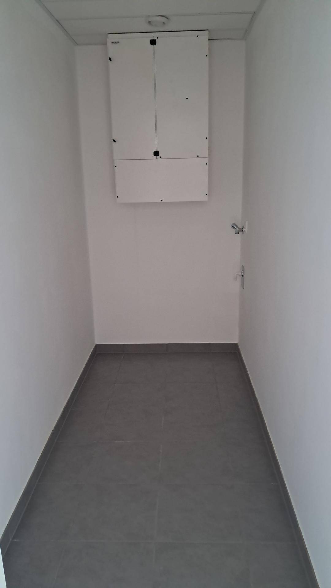 Schmaler Hauswirtschaftsraum mit grauen Fliesen und einem Sicherungskasten an der Wand.