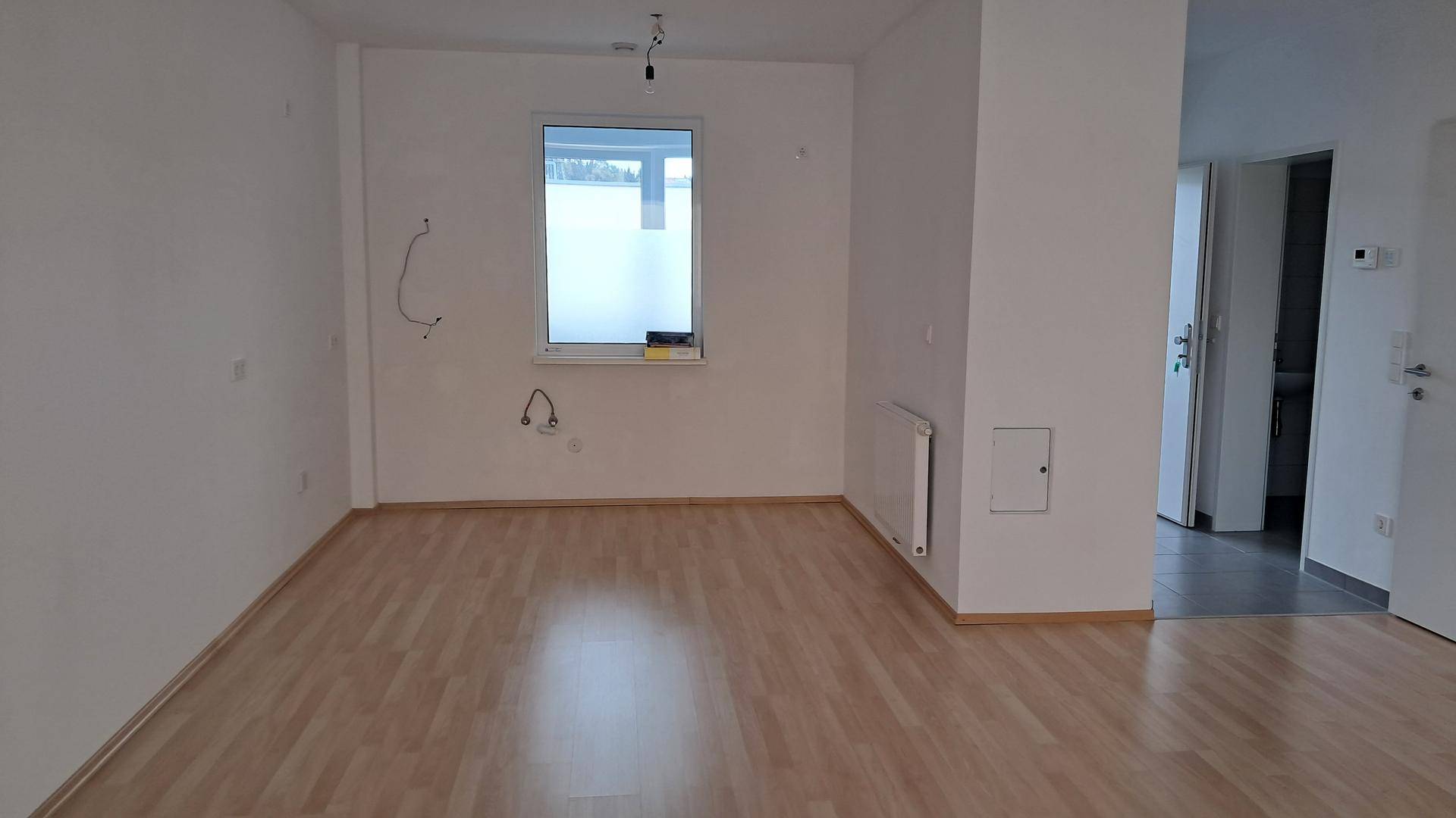 Heller Raum mit Laminatboden und Fenster, vorbereitet für eine Kücheninstallation.