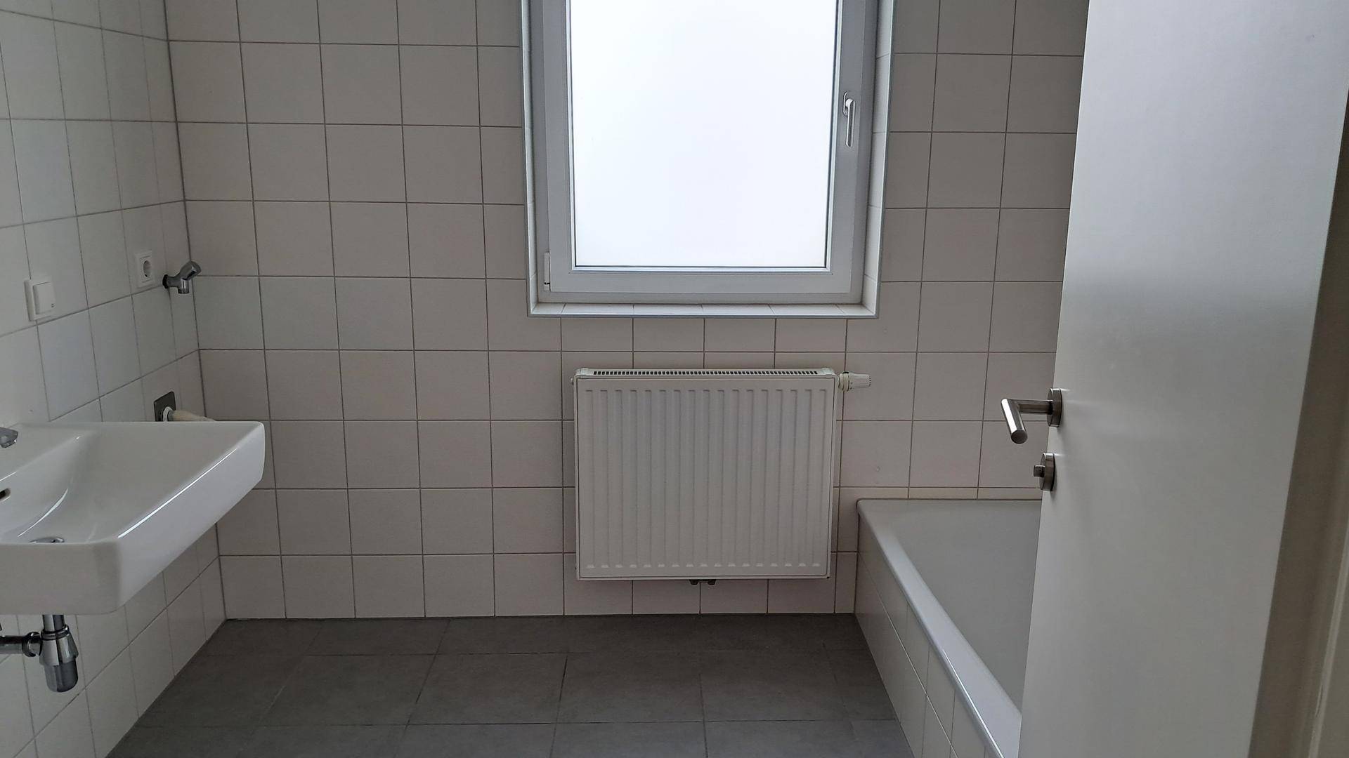 Helles Badezimmer mit Badewanne, Waschbecken, WC und weißen Fliesen.