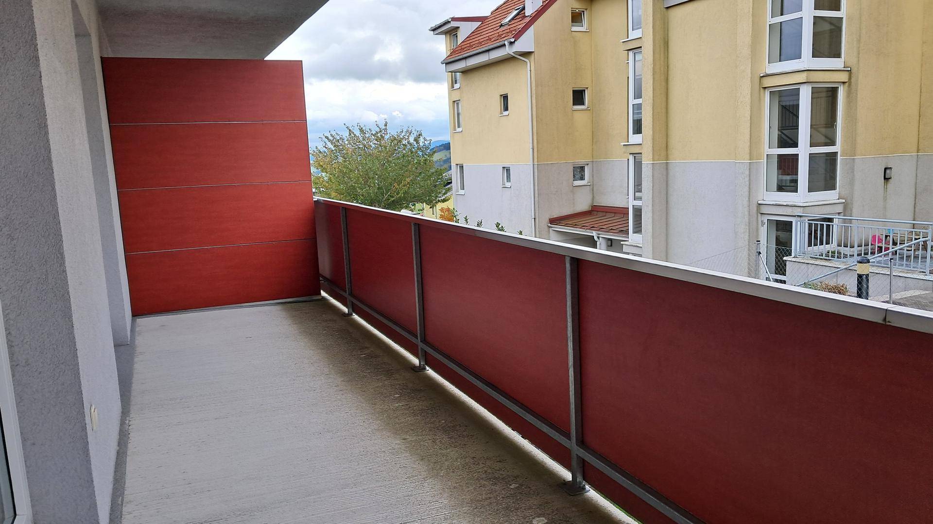 Balkon mit roter Brüstung und Blick auf die umliegenden Gebäude und die Landschaft.