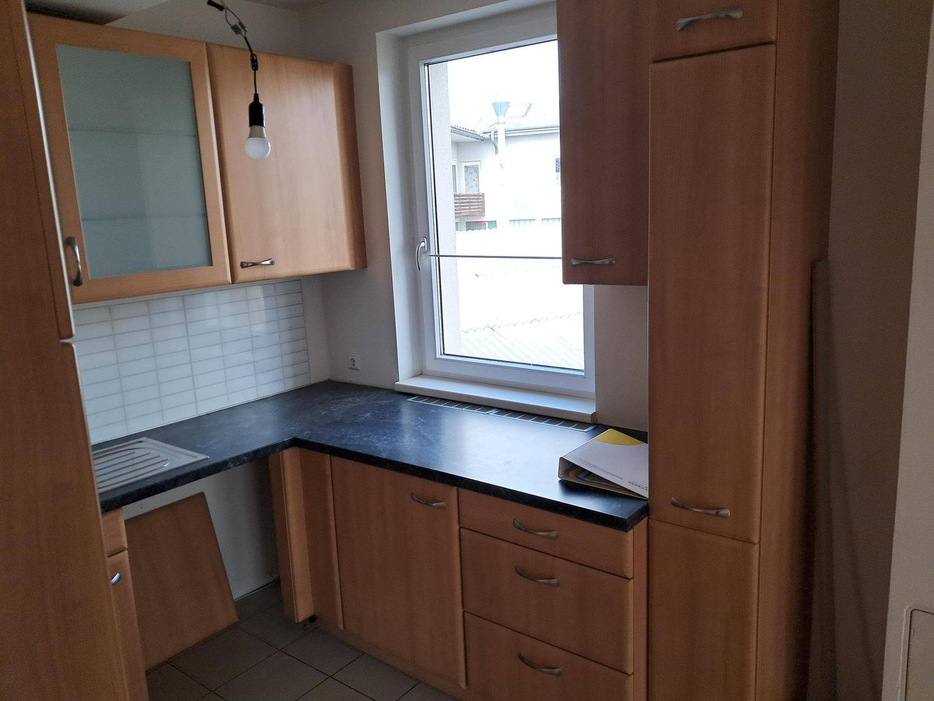 Funktionale Einbauküche mit hellen Holzschränken, dunkler Arbeitsplatte und einem Fenster.