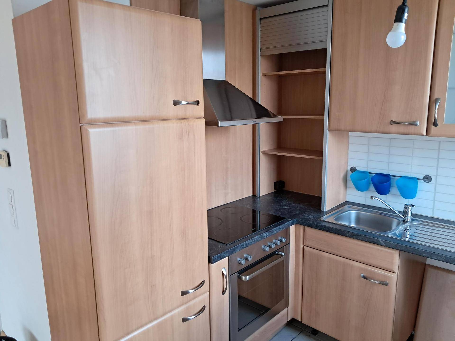 Küche mit Holzfronten, integriertem Herd, Dunstabzugshaube und offenem Regalbereich.