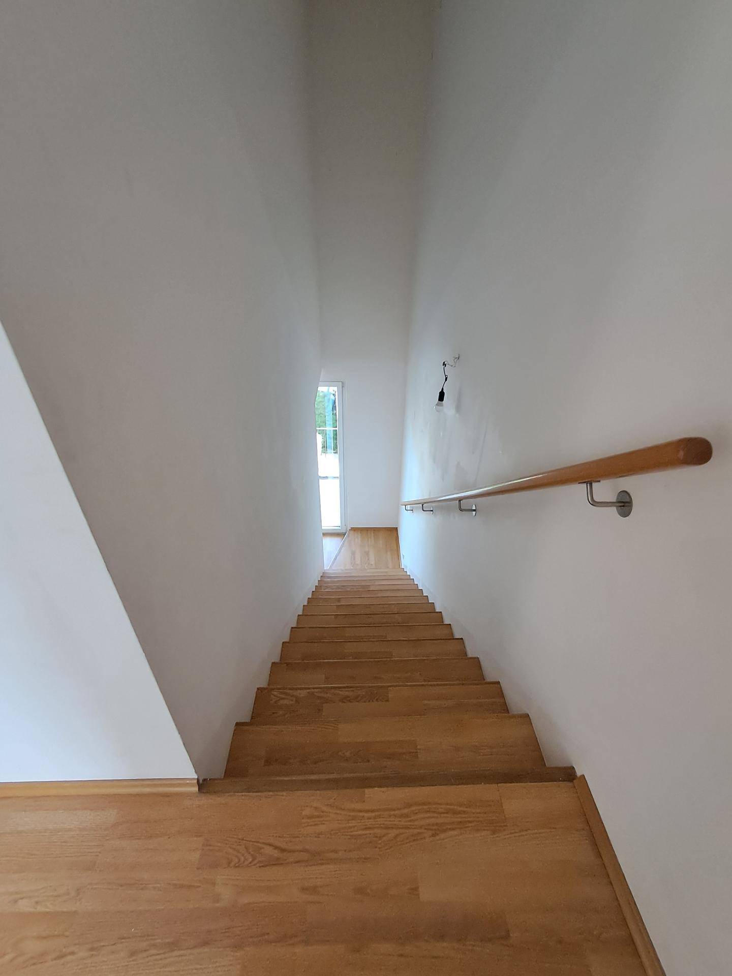 Helle Holztreppe mit einem stabilen Handlauf, die zu einem oberen Bereich führt.