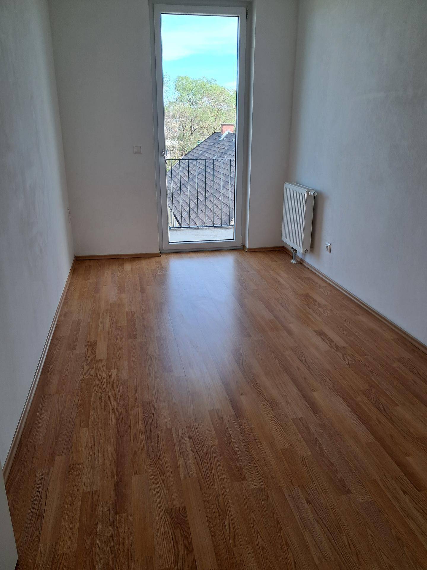 Helles Schlafzimmer mit Laminatboden und einer Fenstertür, die zu einem französischen Balkon führt.
