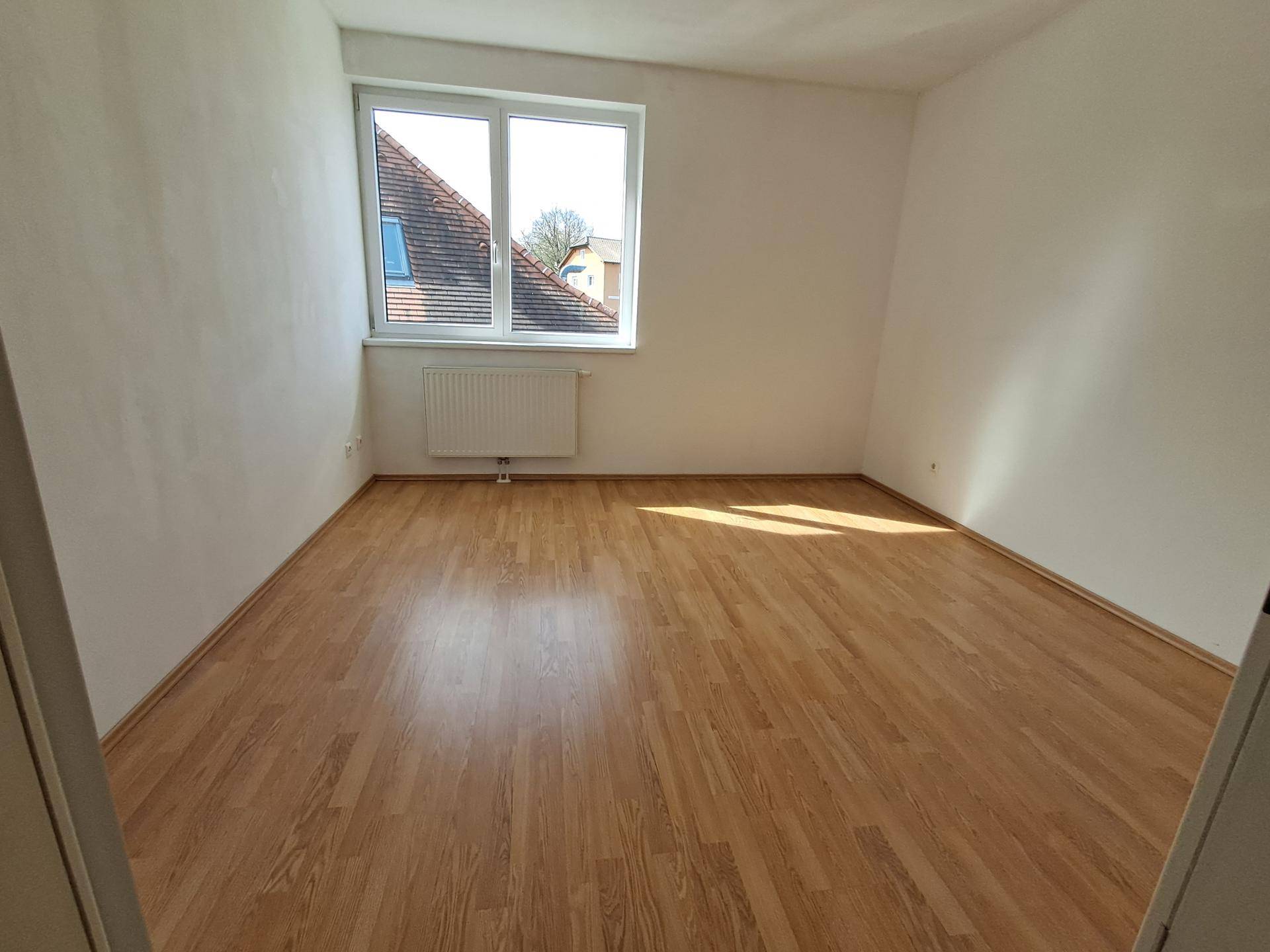 Helles Schlafzimmer mit Laminatboden und einem Fenster, das einen Blick auf die Dächer bietet.