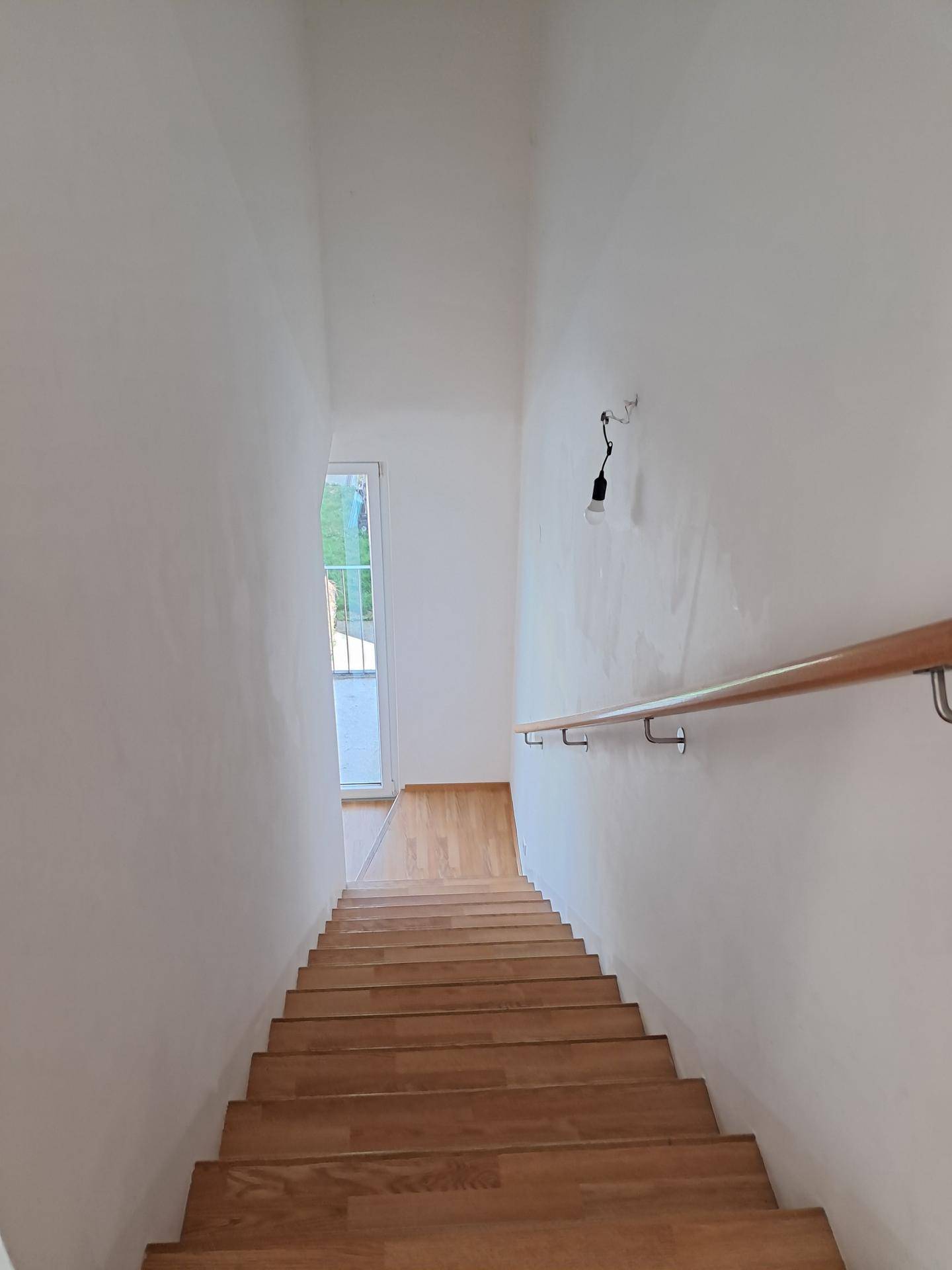 Helle Holztreppe mit Handlauf, die in den unteren Bereich führt und gut beleuchtet ist.