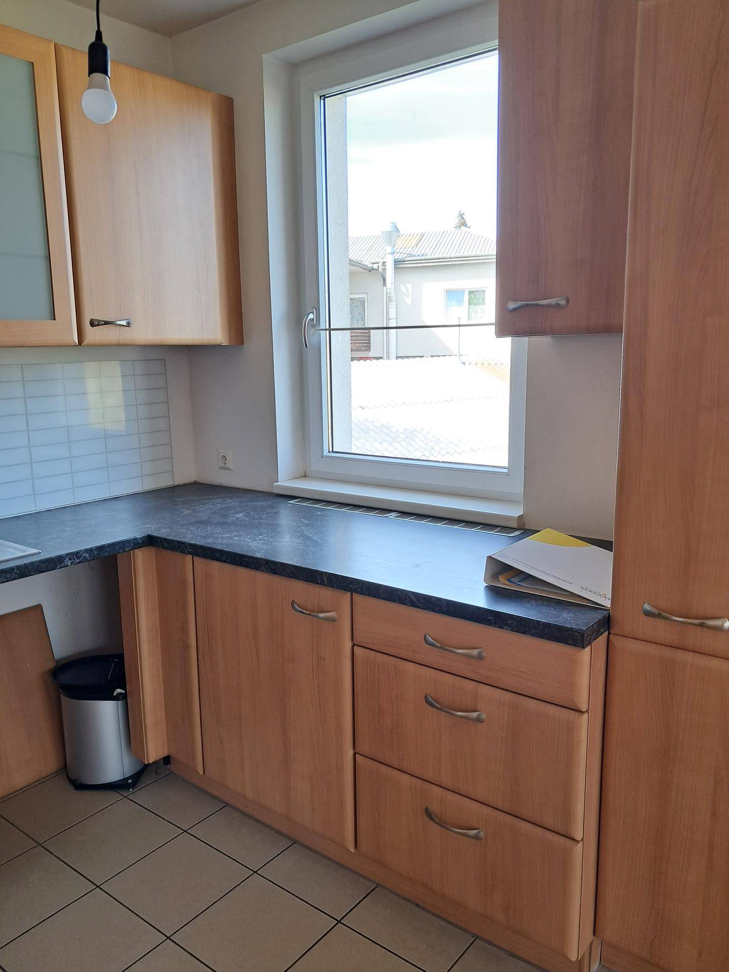 Küchenzeile mit Spülbecken, dunkler Arbeitsplatte und einem Fenster, das Tageslicht hereinlässt.