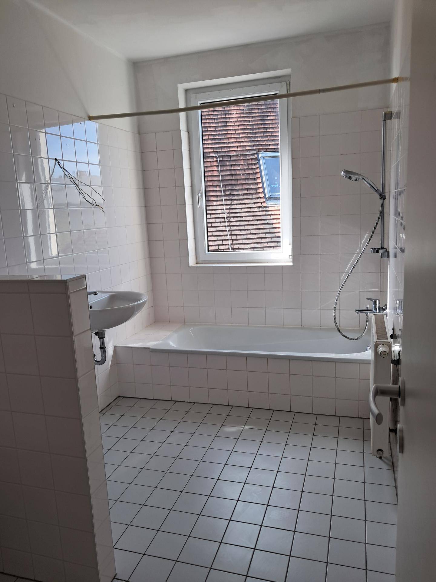 Helles Badezimmer mit weißen Fliesen, Badewanne, Dusche und einem Fenster für natürliche Belüftung.