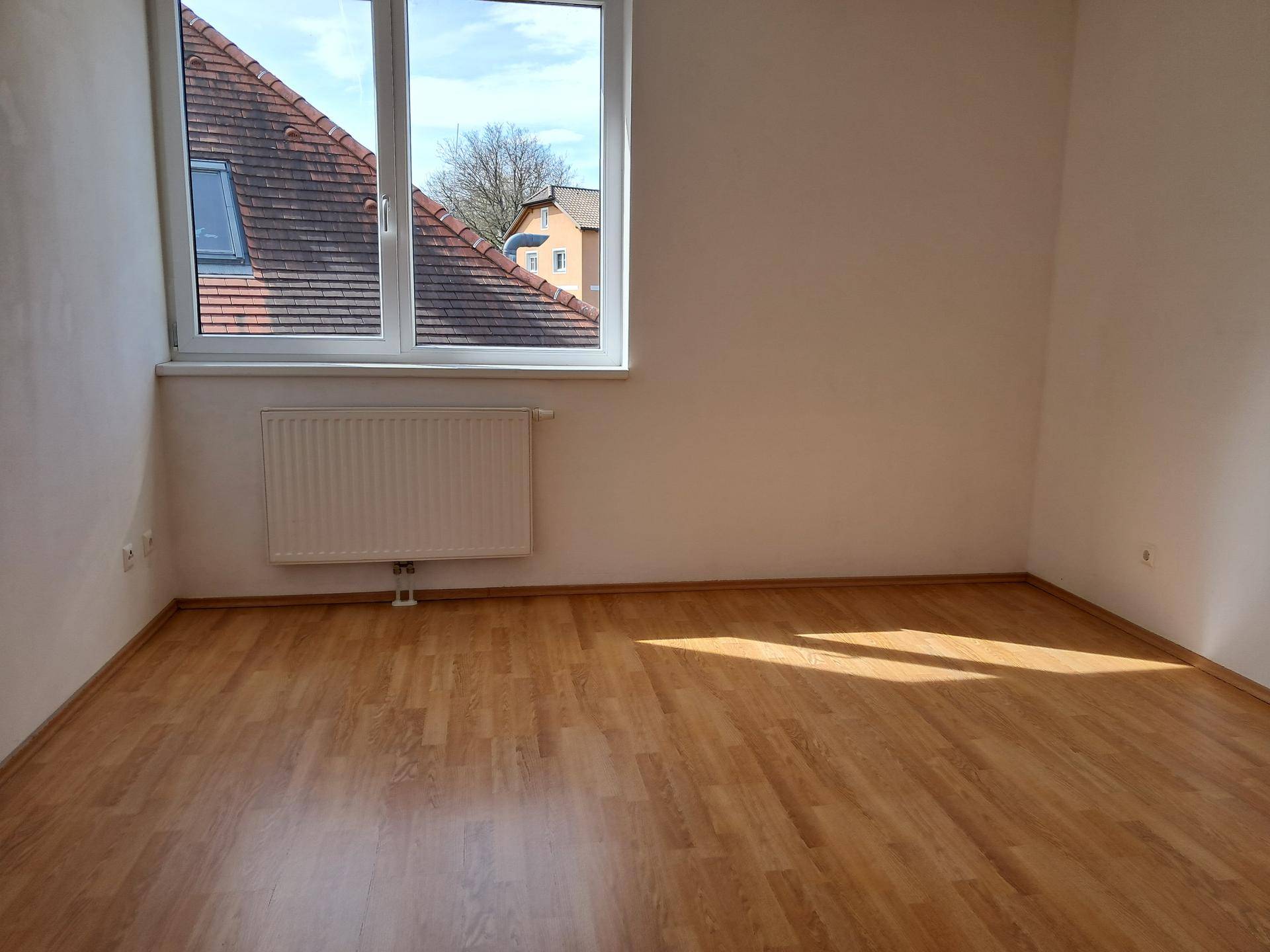 Helles Schlafzimmer mit Laminatboden und einem Fenster, das einen Blick auf die Dächer bietet.