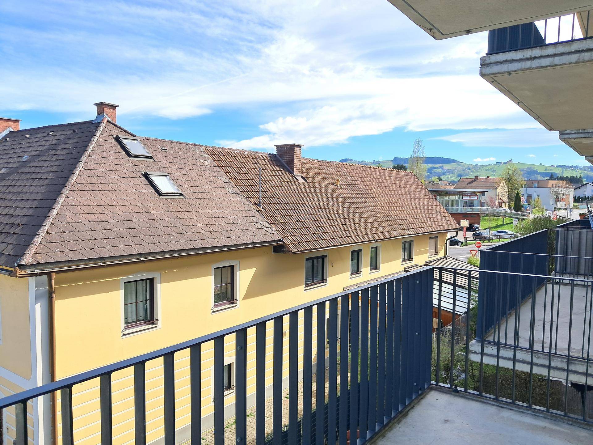 Balkon mit Blick auf ein benachbartes Gebäude und die umliegende Landschaft unter blauem Himmel.