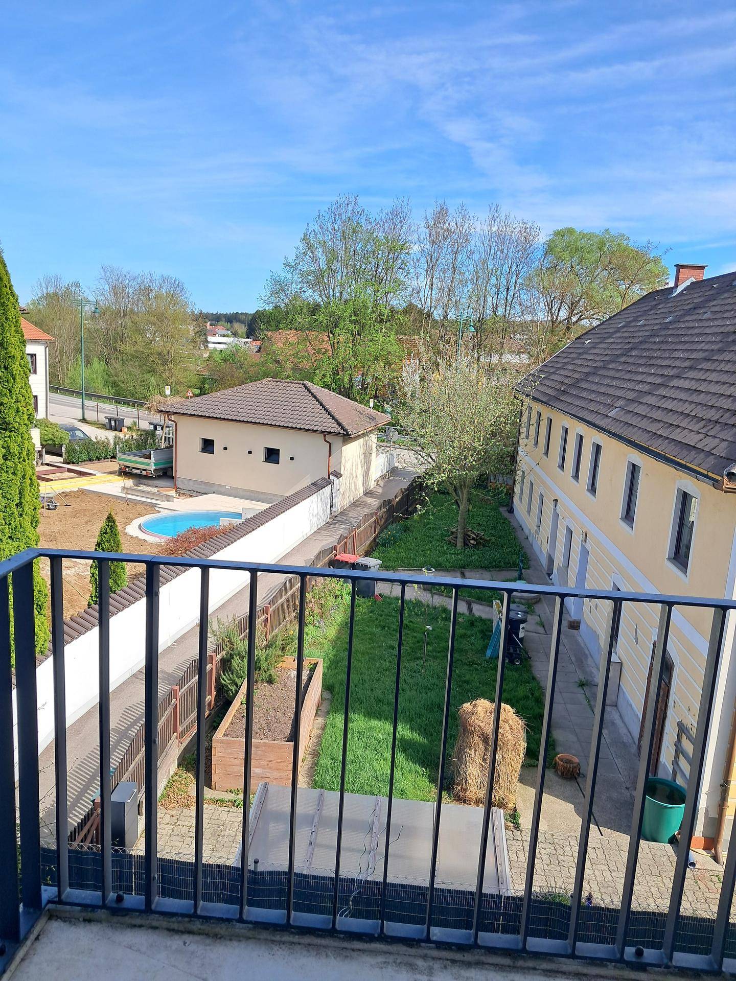 Balkon mit Blick auf einen Gartenbereich und einen Pool in der Nachbarschaft unter blauem Himmel.