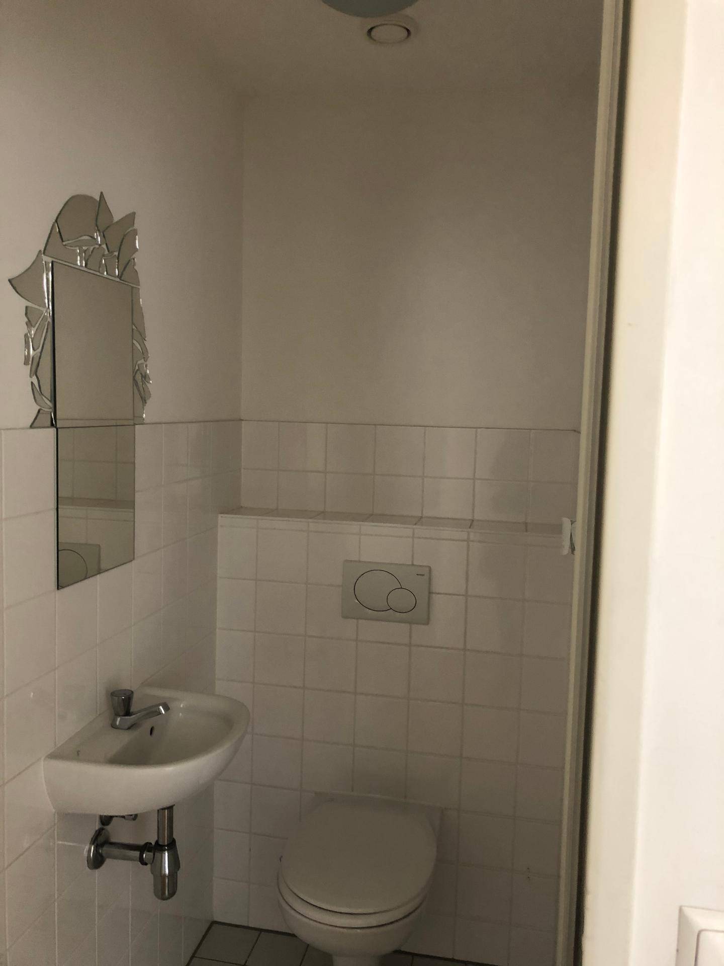 Kleines Gäste-WC mit weiß gefliesten Wänden, wandhängendem WC und einem Waschbecken.