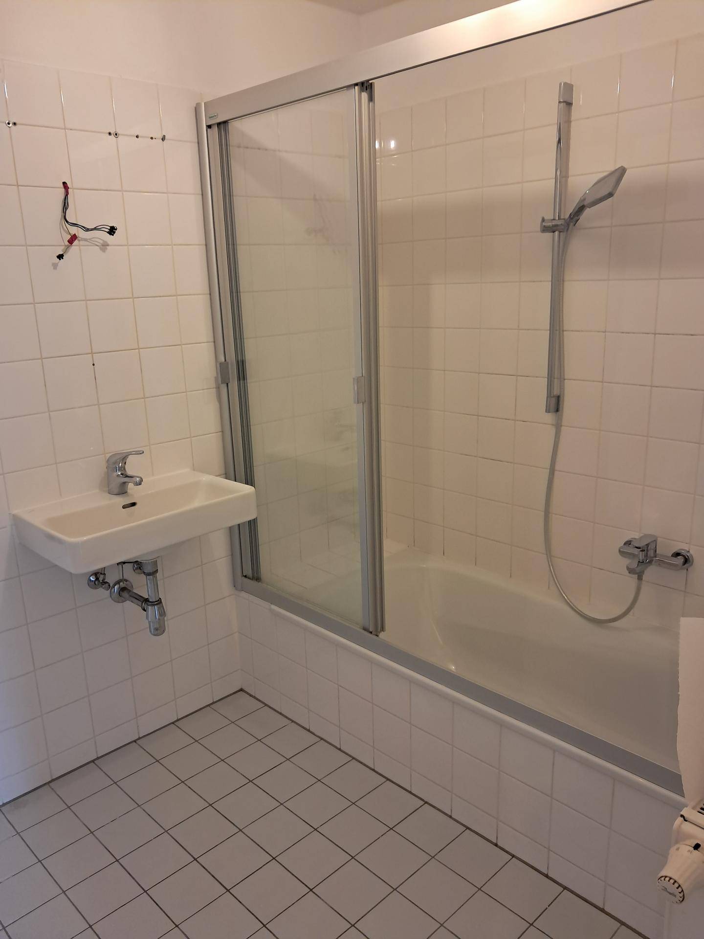 Badezimmer mit Badewanne inklusive Duschfunktion, Waschbecken und weißen Wandfliesen.