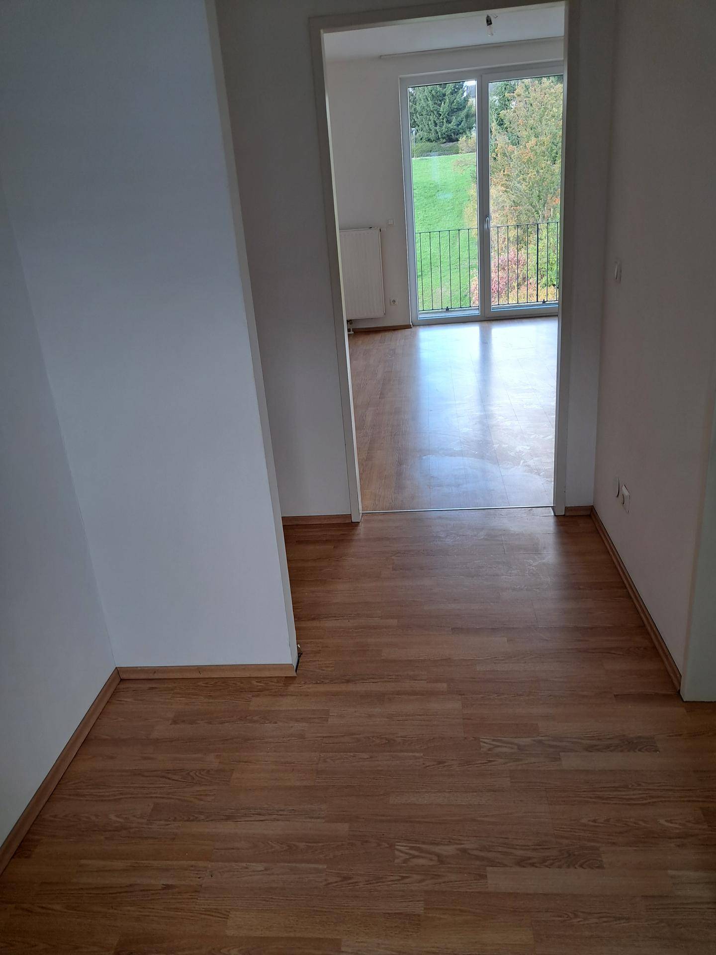 Heller Flur mit Holzboden, der zu einem weiteren Zimmer mit Balkonzugang führt.
