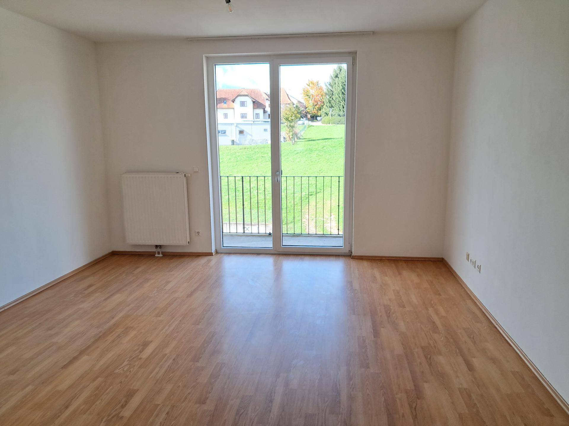 Helles Zimmer mit Holzboden und großem Fenster, das einen weiten Blick ins Grüne bietet.