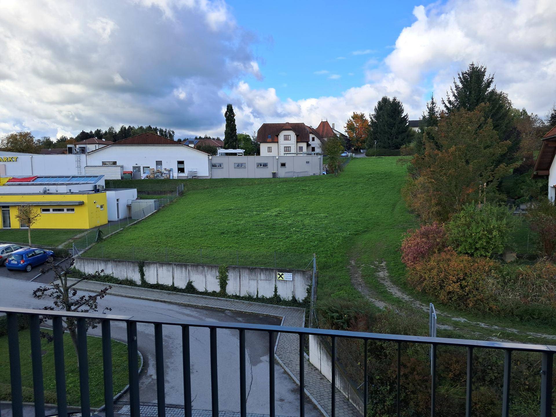 Weitläufiger Blick von einem Balkon auf eine grüne Hügellandschaft und umliegende Gebäude.