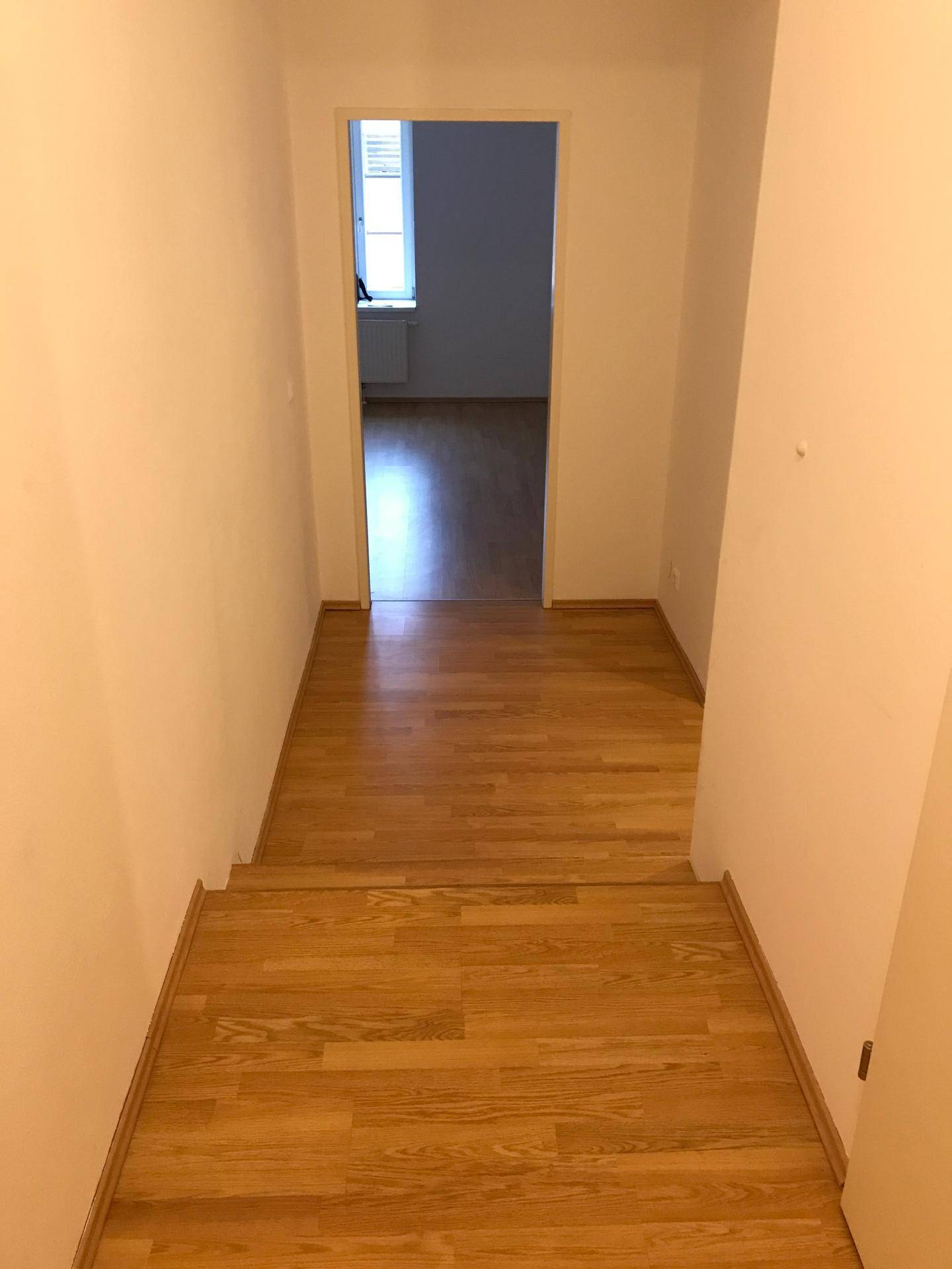 Heller Flur mit Holztreppe und Laminatboden, der zu einem oberen Bereich führt.