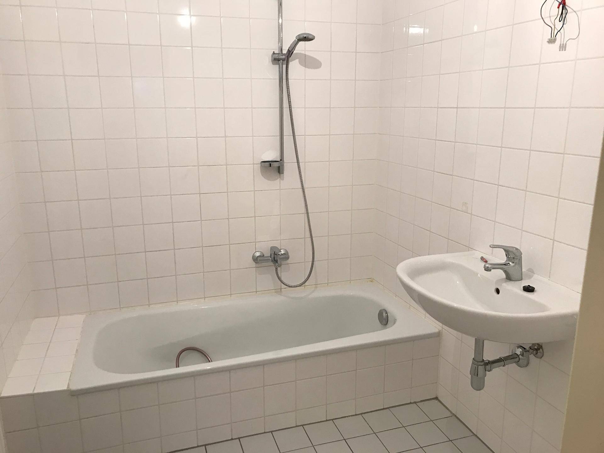 Badezimmer mit weiß gefliesten Wänden, Badewanne und einem einzelnen Waschbecken.