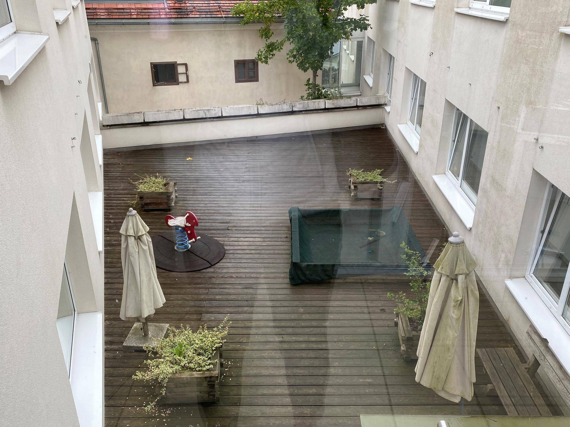 Innenhof mit Holzterrasse, Sonnenschirmen und einem kleinen Spielgerät für Kinder.