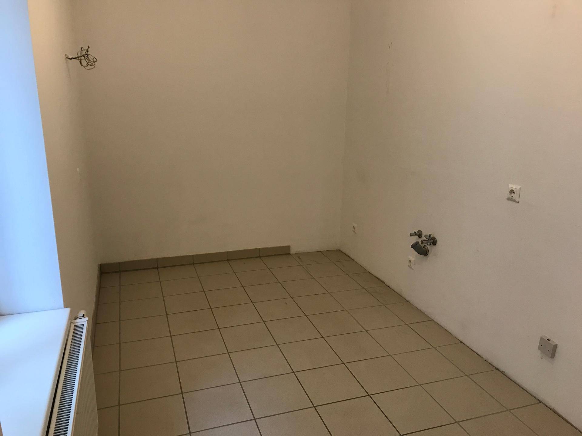 Leerer Raum, vorbereitet für eine Küche, mit Fliesenboden und Anschlüssen für Geräte.