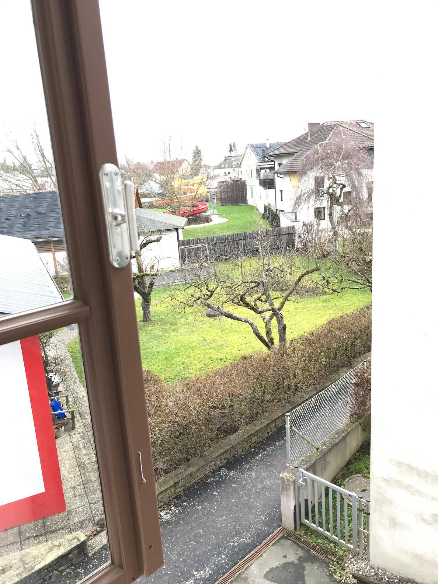 Blick aus dem Fenster auf einen grünen Hinterhof mit Bäumen und einer Hecke.