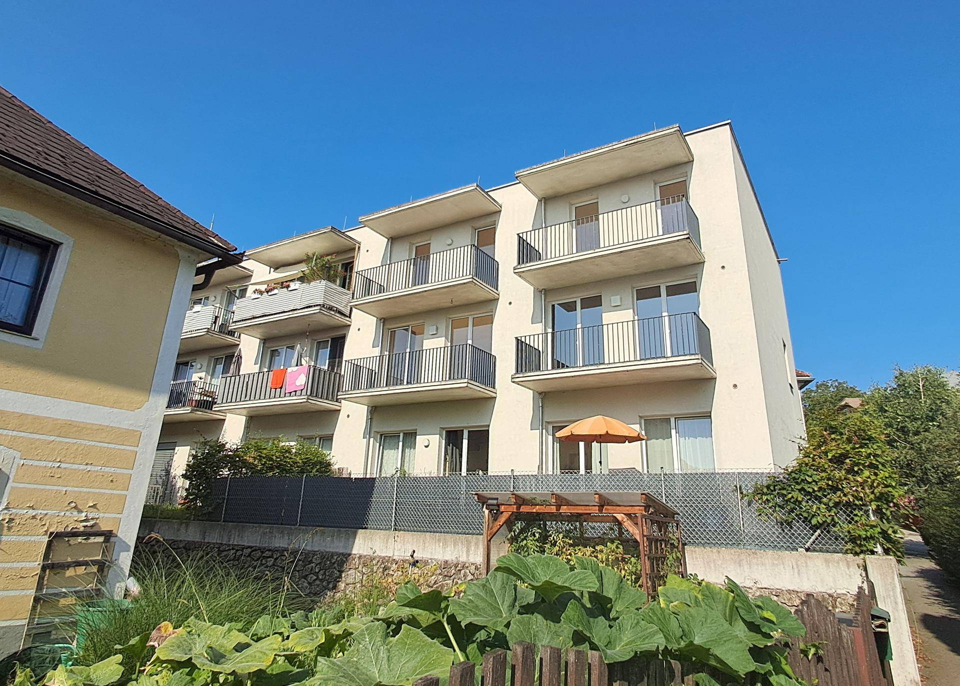 Fassade eines modernen Wohnhauses mit Balkonen und einem kleinen Gartenbereich im Vordergrund.