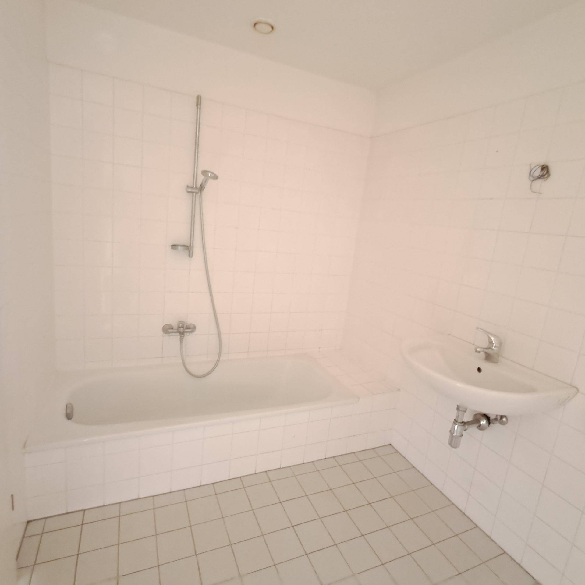 Badezimmer mit weißen Fliesen, einer Badewanne mit Duschfunktion und einem Waschbecken.