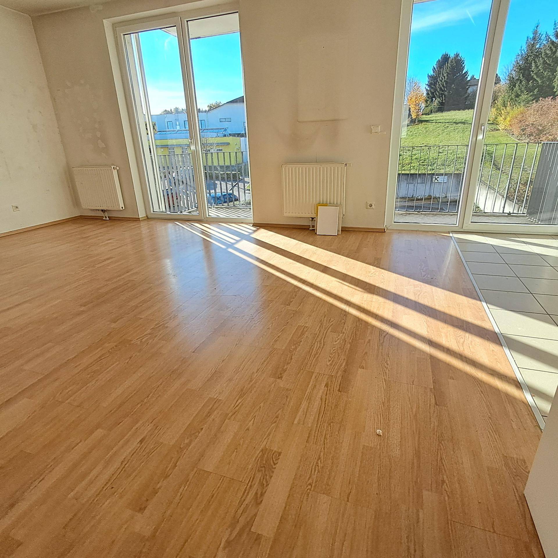 Lichtdurchfluteter Wohnbereich mit Laminatboden und Fliesen, großen Fenstern und Balkonzugang.