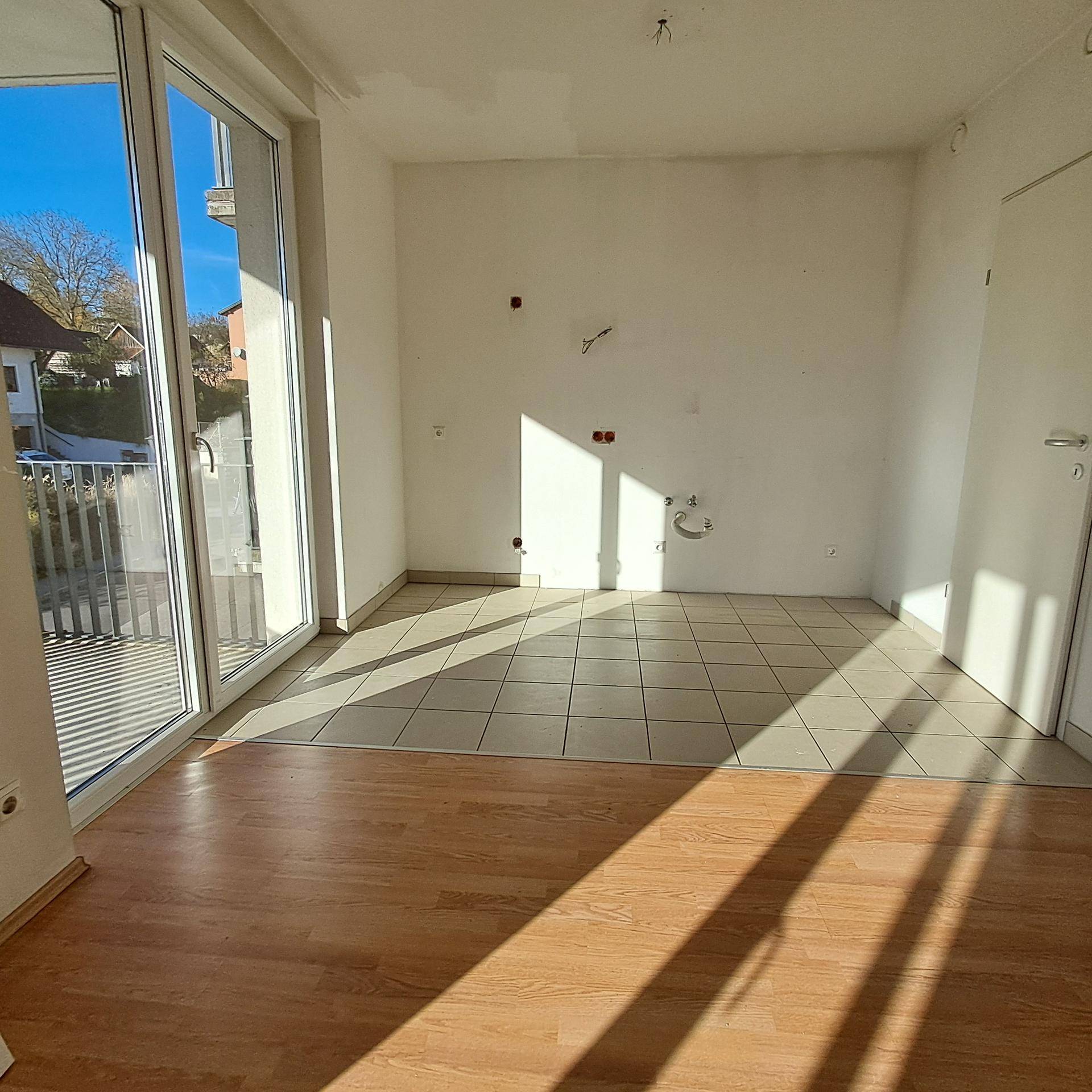 Heller Raum mit Fliesen- und Laminatboden, großen Fenstern und Zugang zu einem Außenbereich.