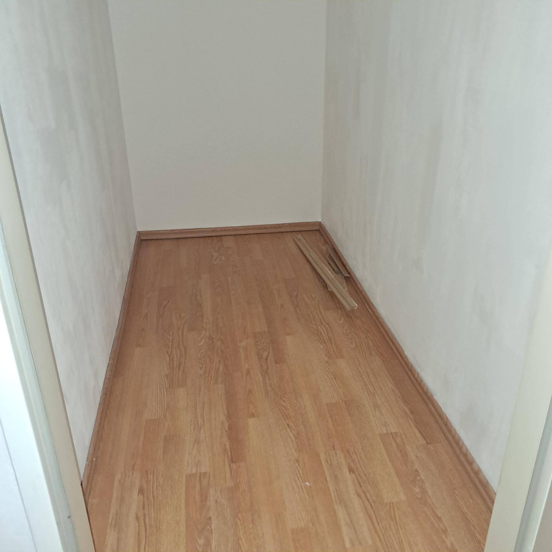 Schmaler Abstellraum mit hellem Laminatboden und weißen Wänden, bereit zur Nutzung.