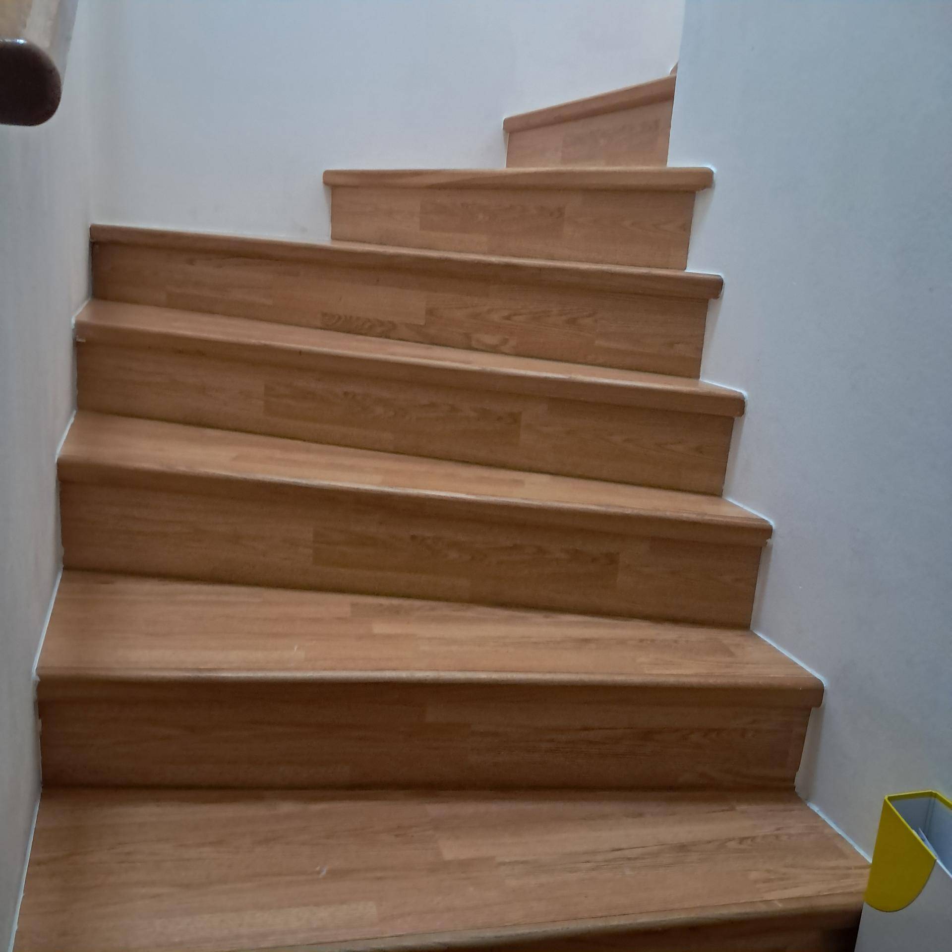 Holztreppe mit hellen Stufen und weiß gestrichenen Wänden, die in die obere Etage führt.